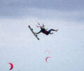 Kitesurfer fliegt auf Wellen und hält sein Kiteboard in seiner linken Hand - Kite2Connect